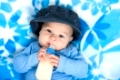 happy baby with feeding bottle and baseball cap on a blue baby blanket.; 

glückliches Baby mit Nuckelflasche und Basecap auf einer blauen babydecke.